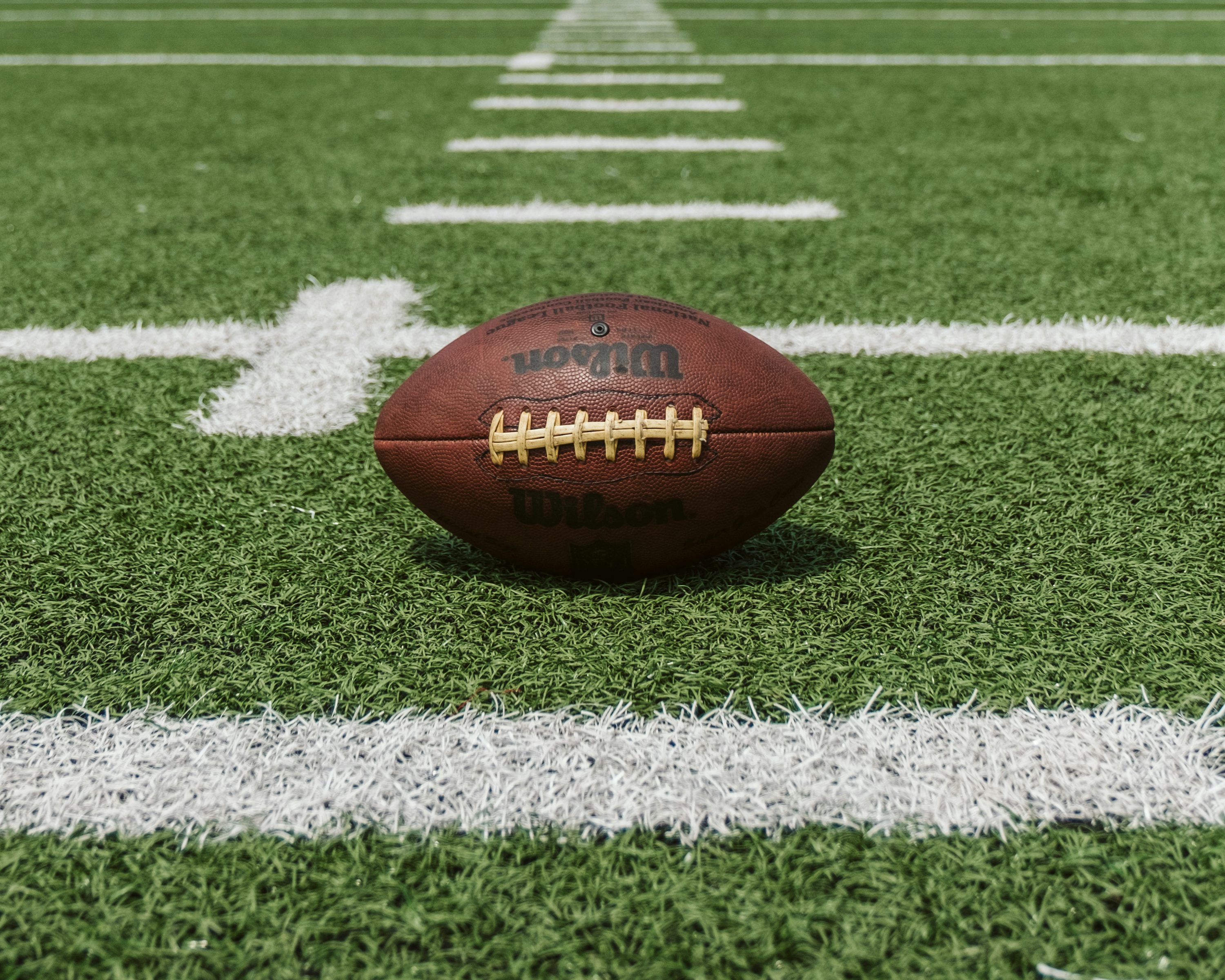 American football lying on the green turf field near a white yard line marker.