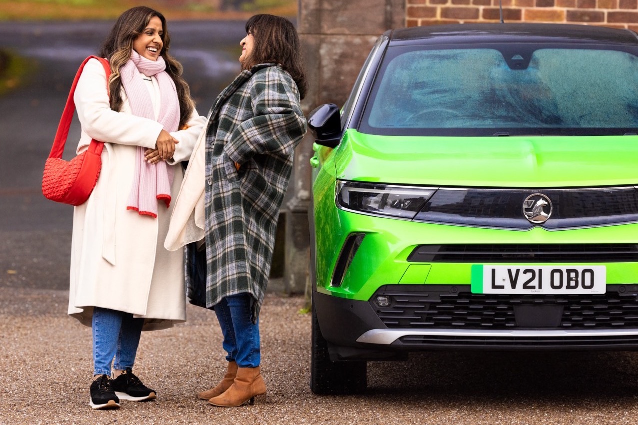Two people talking beside a green car