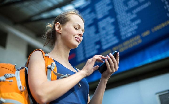 woman looking at her phone in front of a destination board
